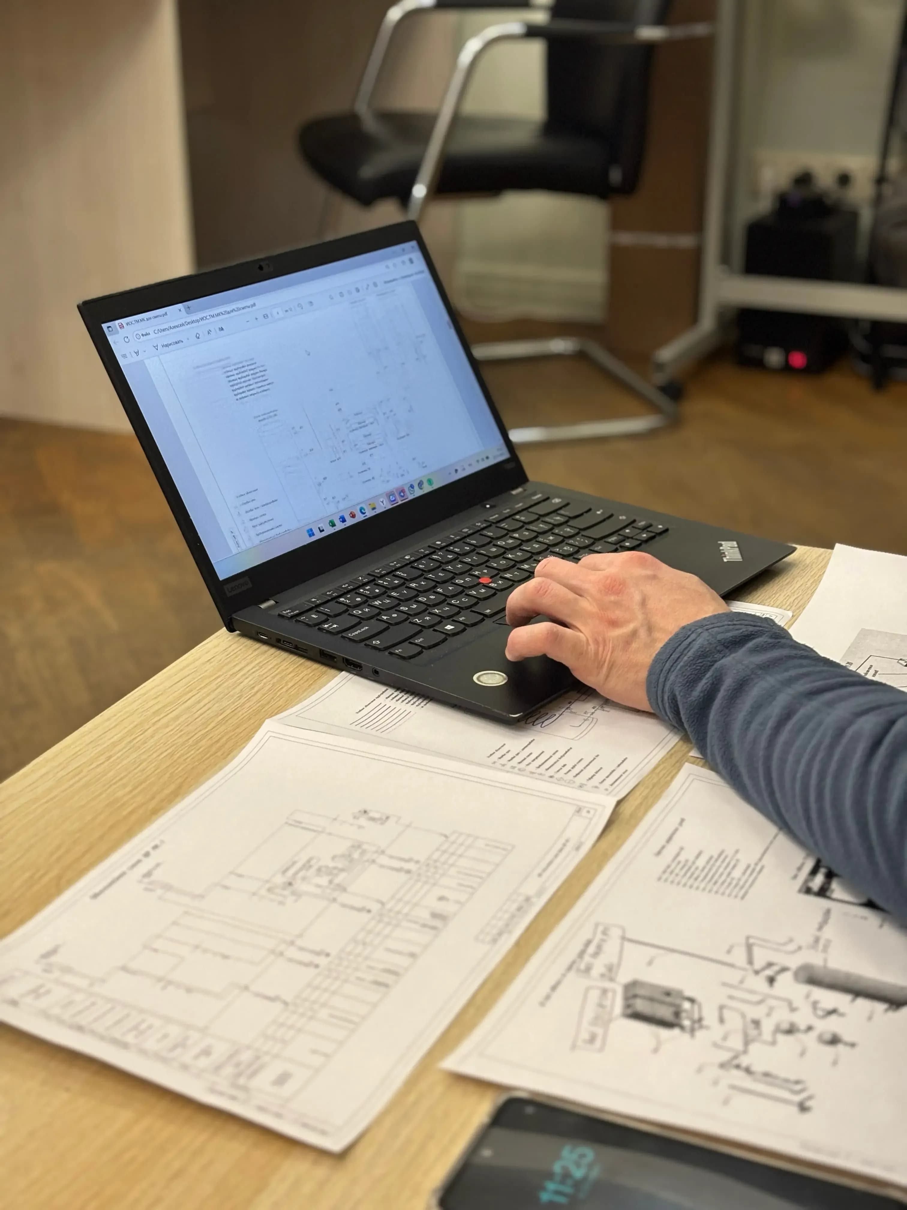 Ingenieur bearbeitet einen elektrischen Schaltplan am Laptop mit ausgedruckten Plänen